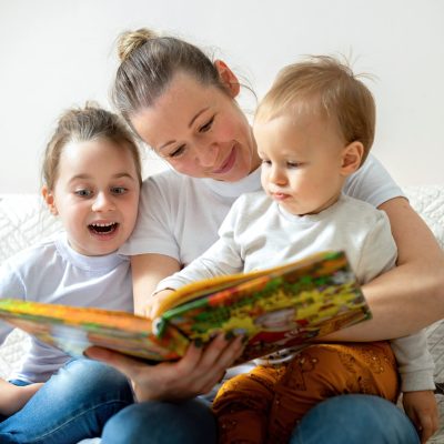 Mom and her two children are reading a book at home on a sofa. Happy and smiling